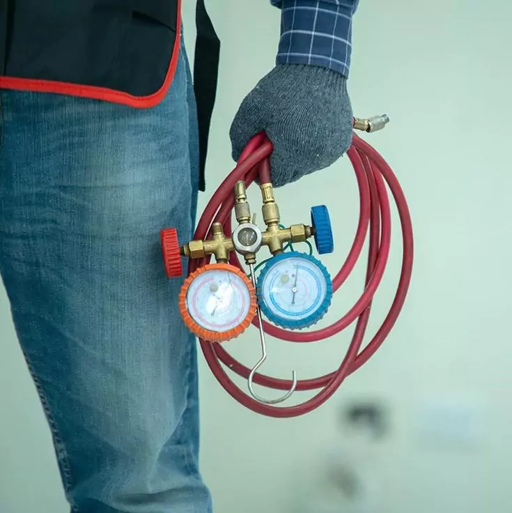 فني تكييف يحمل مقاييس ضغط الفريون مع الخراطيم، جاهز لخدمة إصلاح وتعبئة غاز المكيف في الكويت.