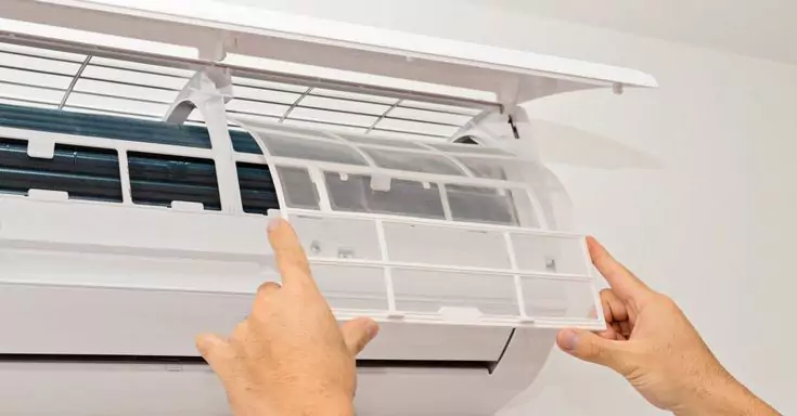 يدان تسحبان فلتر هواء نظيفًا من وحدة تكييف سبليت داخلية مفتوحة، توضح فحص وصيانة فلتر المكيفات الروتينية لتحسين جودة الهواء في الكويت.