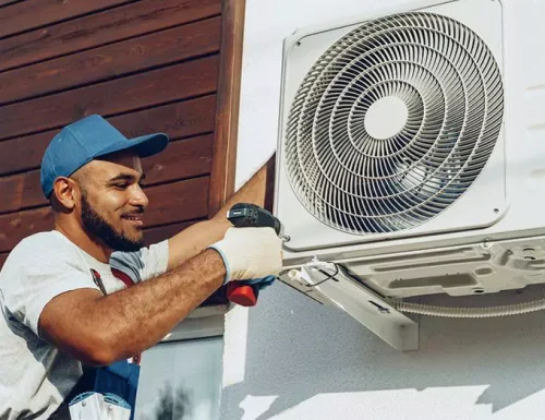 فني مبتسم يستخدم مثقابًا كهربائيًا لتركيب وحدة تكييف خارجية.