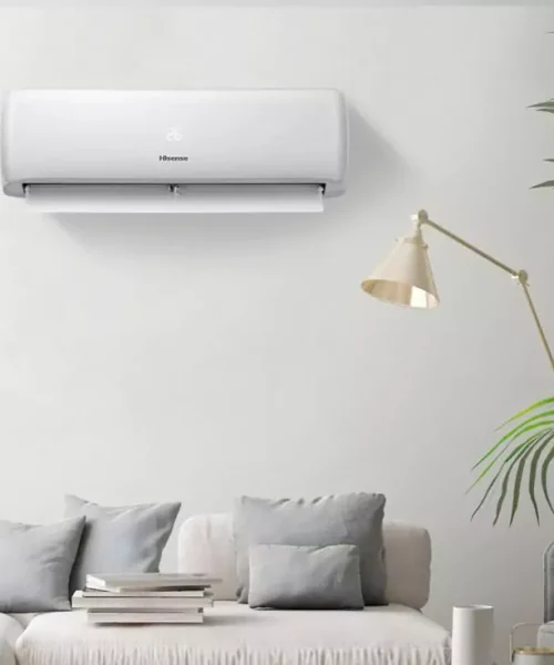 وحدة تكييف هايسنس إيكو سمارت بيضاء أنيقة مثبتة على جدار غرفة معيشة عصرية فوق أريكة بيضاء بوسائد ومصباح جانبي، تصور الراحة والمكيفات الحديثة في الكويت.