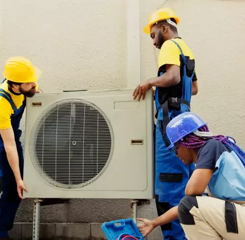 فريق مكون من ثلاثة فنيين مهرة يرتدون خوذات وملابس عمل، يتعاونون لتركيب وحدة تكييف هواء خارجية في الكويت.